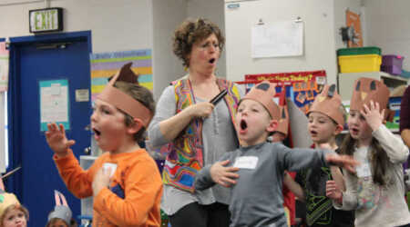 Noa Baum and young students march and open their mouths wide during a workshop.