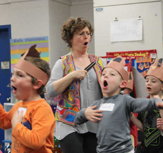 Noa Baum and young students march and open their mouths wide during a workshop.