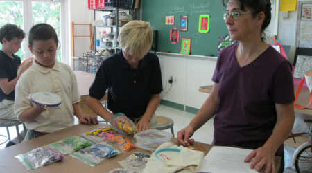 Suzanne Herbert-Forton and students stand at a desk with art supplies.