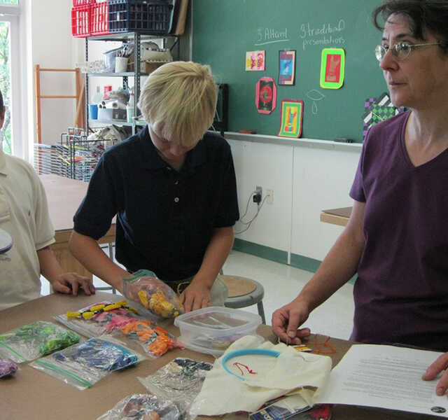 Suzanne Herbert-Forton and students stand at a desk with art supplies.