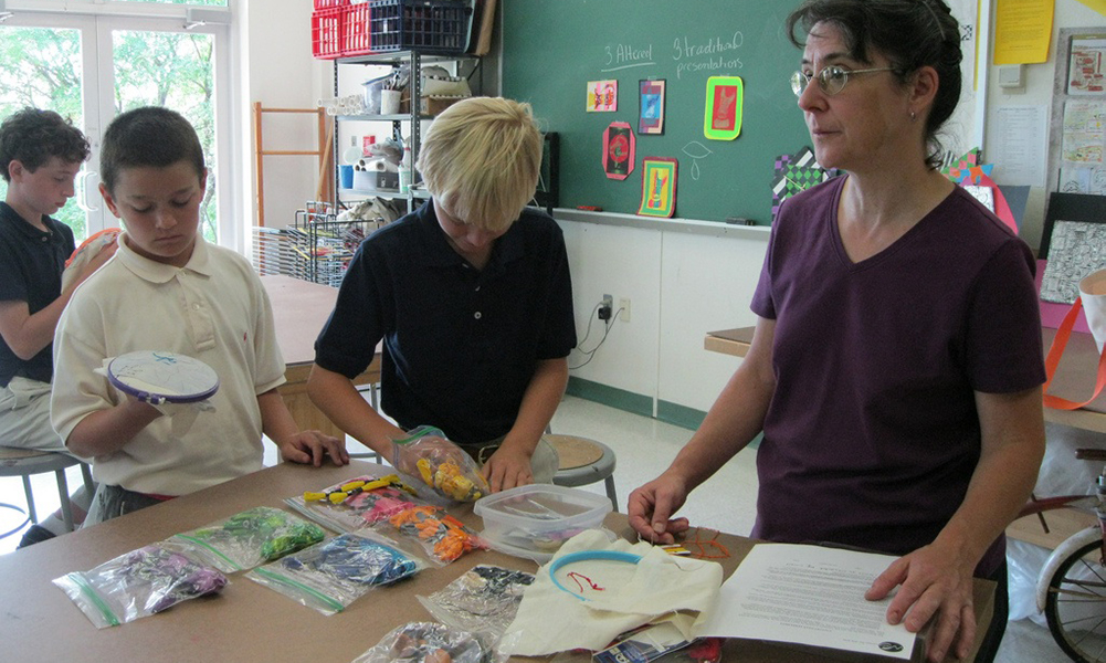 Suzanne Herbert-Forton and students stand at a desk with art supplies.