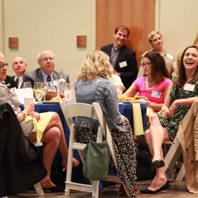 Guests smiling and laughing as they gathered around tables set with a delicious breakfast of fruit, juice, biscuits, and candied bacon.