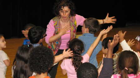 Noa Baum gestures dramatically with a group of young students.