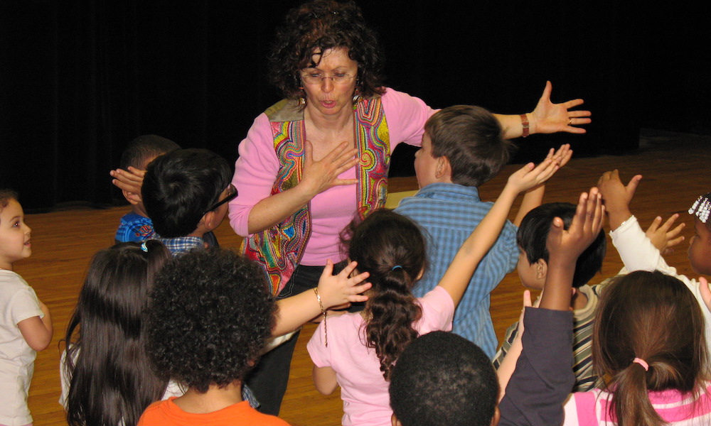 Noa Baum gestures dramatically with a group of young students.