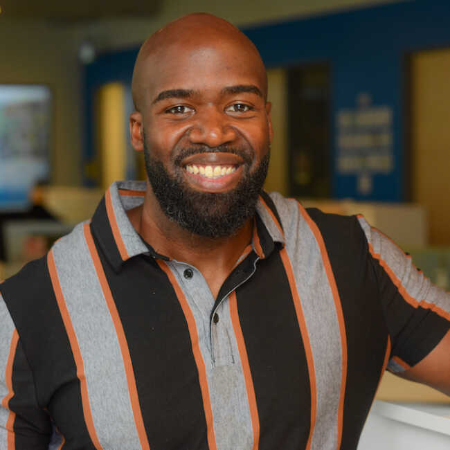 A close-up photograph of DJ Brooks standing in the office space