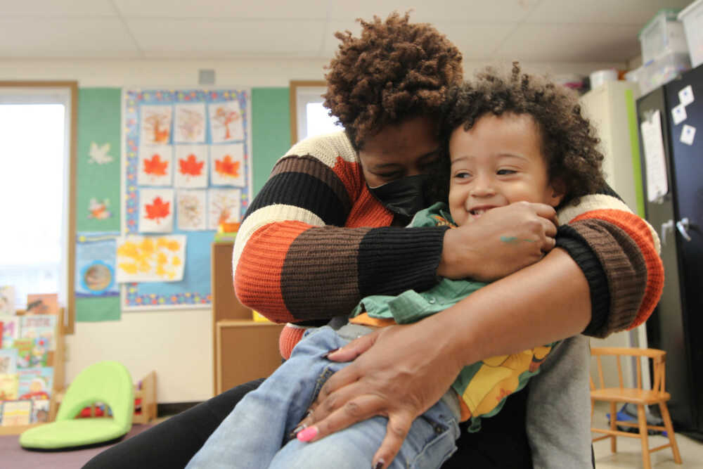 Adult hugging and holding a smiling toddler on her lap.