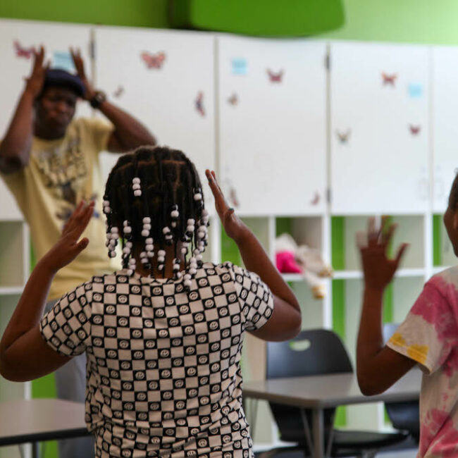 Students mimic movements of teaching artist standing at the back of the classroom.