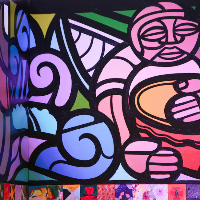 A mural painted in pinks, blues, violets, and greens shows a figure