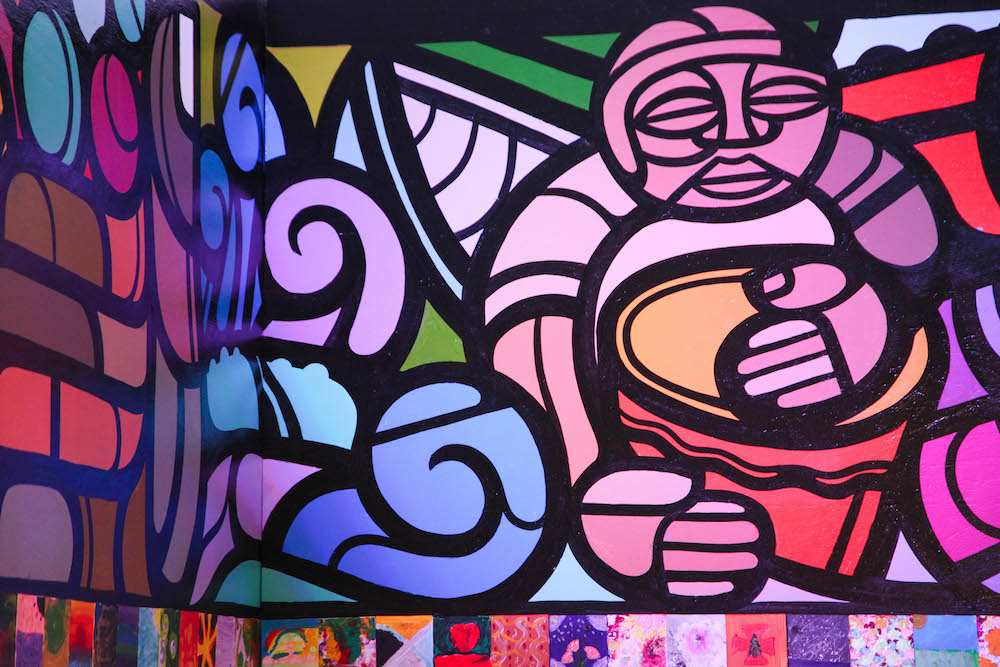 A mural painted in pinks, blues, violets, and greens shows a figure