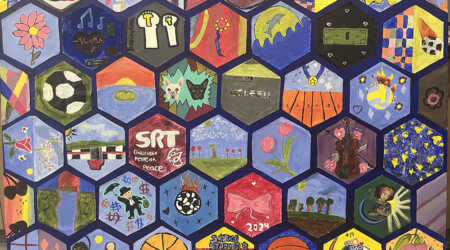 Multiple hand-painted hexagons by children are arranged on a blue background.