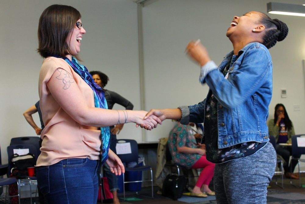 Profile view of two adults shaking hands, laughing and smiling.