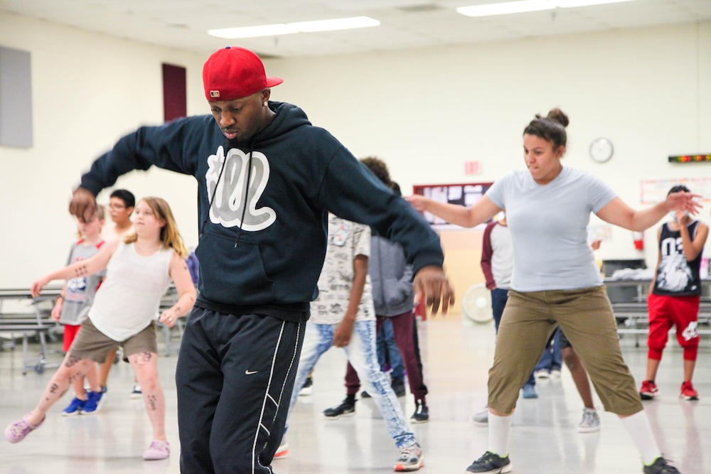 In a red cap and black sweatshirt, an ensemble member of Illstyle & Peace leads students in Hip Hop dance instruction.