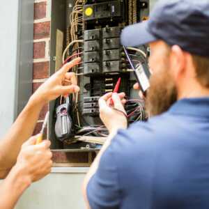 electricians checking electrical panel breakers with meter