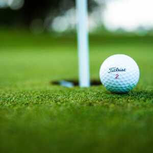 Golf ball on green near golf pin and hole