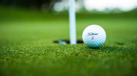 Golf ball on green near golf pin and hole