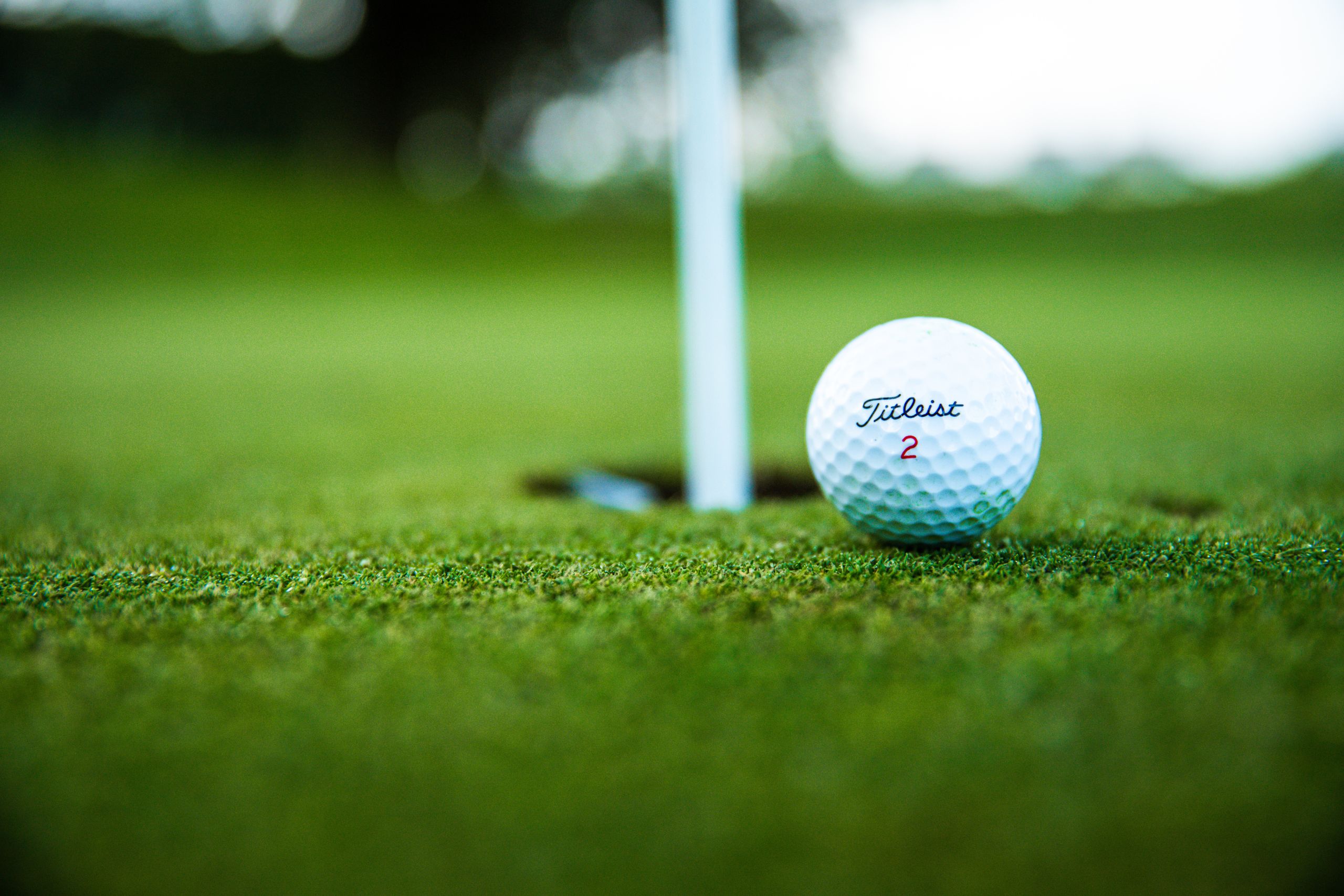 Golf ball on green near golf pin and hole