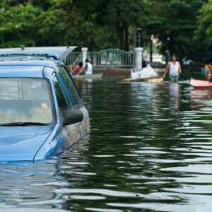 pickup truck in flooded road with water up to the door handles and people and row boat in background