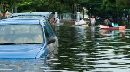 pickup truck in flooded road with water up to the door handles and people and row boat in background