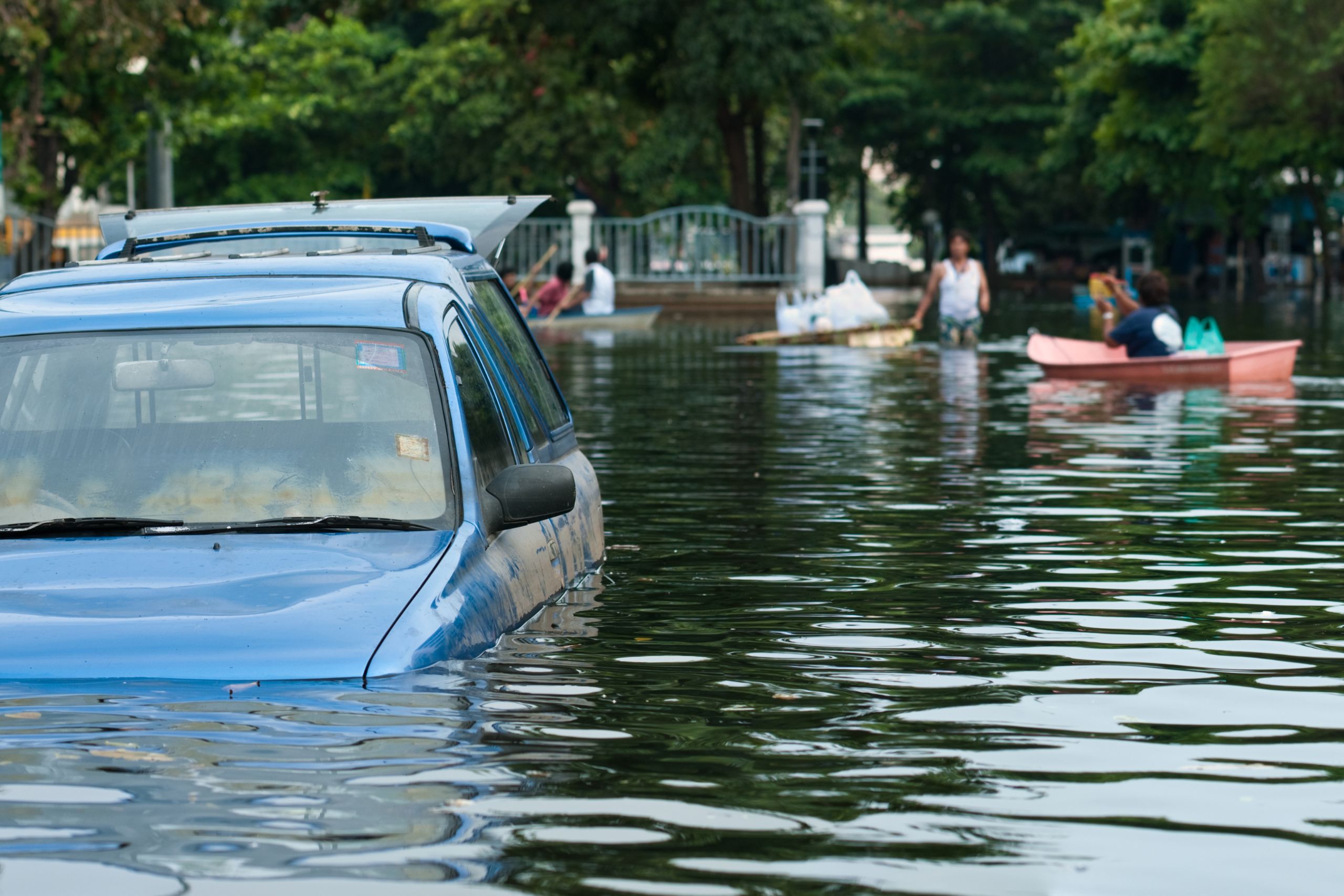 pickup truck in flooded road with water up to the door handles and people and row boat in background