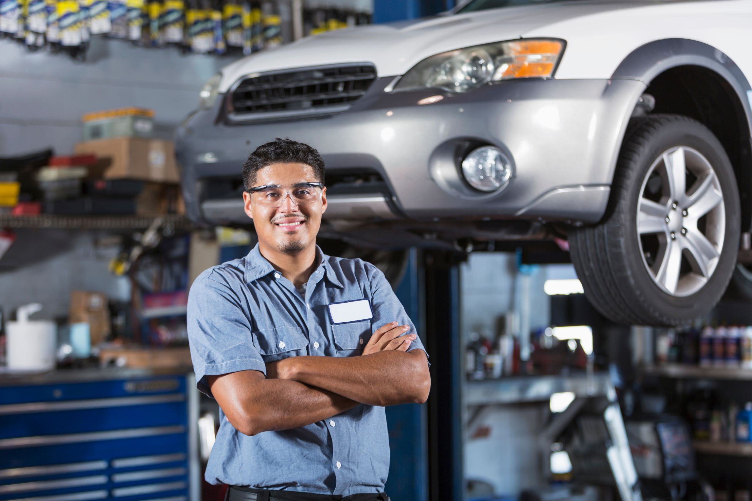auto service technician standing in front of car on a lift with a toolbox behind it