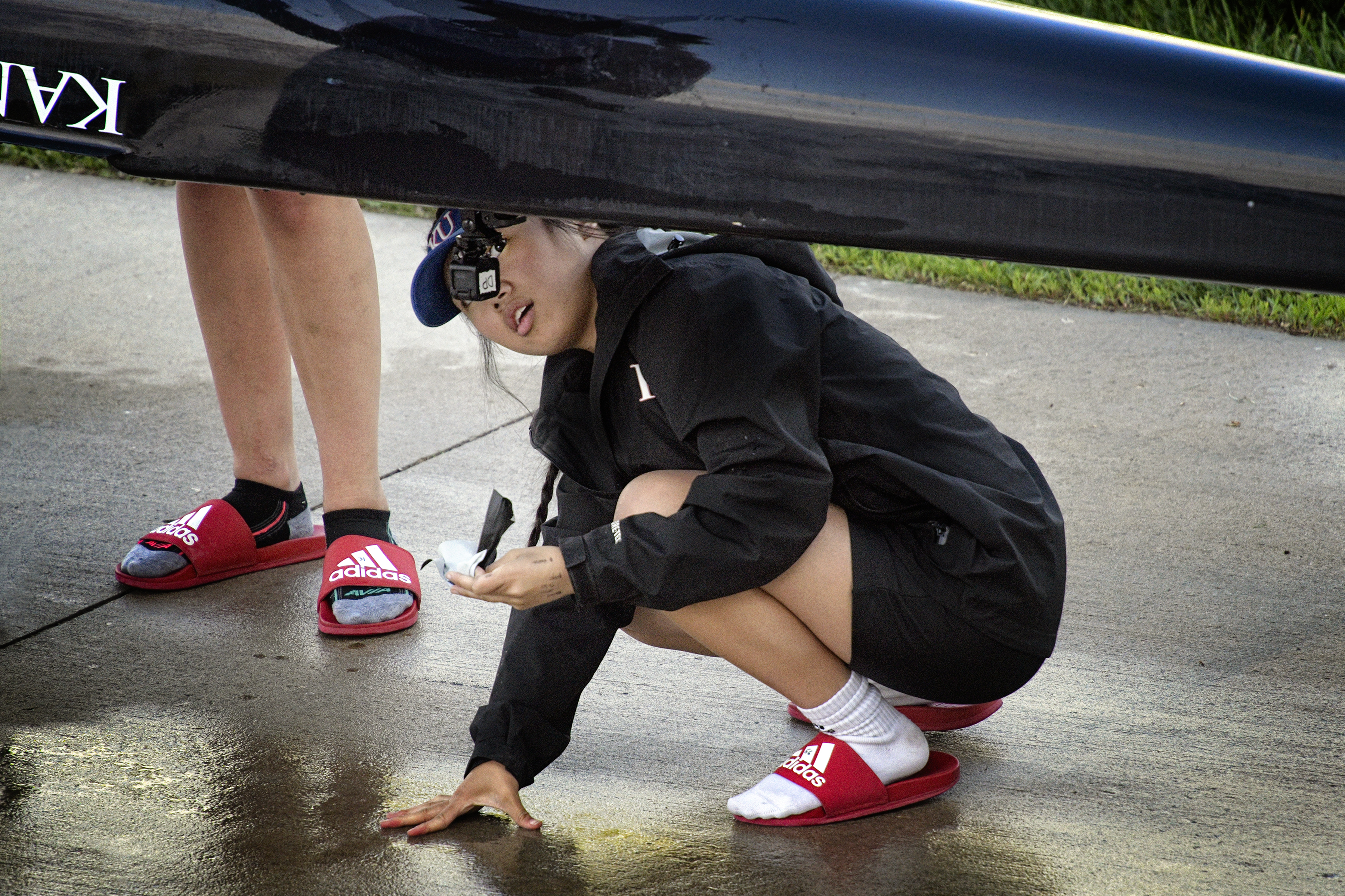 CAMERA CHECK – KU FR coxswain Danica Pecana checked the small video camera attached to the boat after the third varsity four race against Creighton at the Kansas Rowing Boathouse on Friday, April 26.