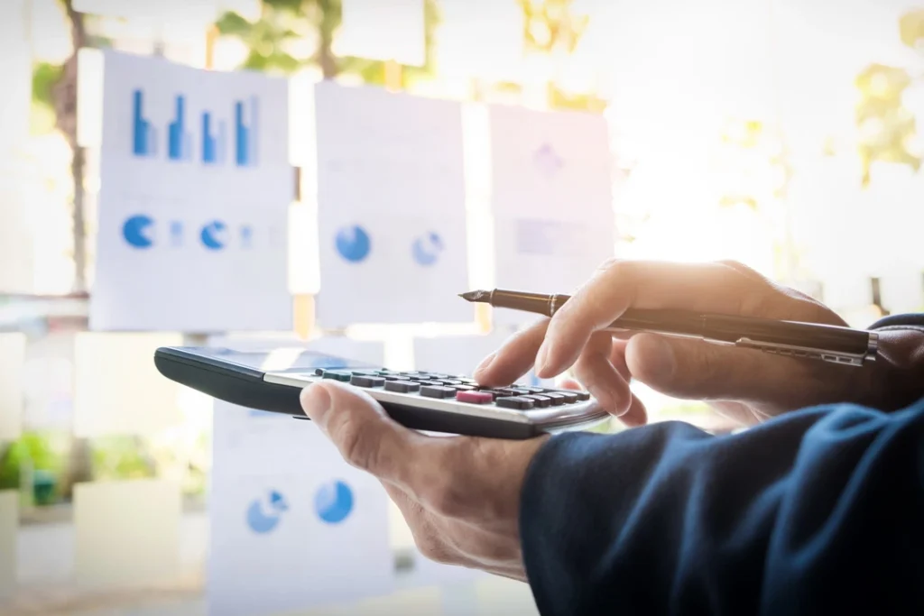 Hands holding a pen and calculator while reviewing pricing data charts