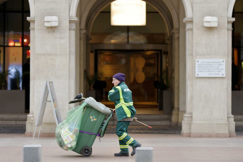 A sanitation worker beside a large dumpster container