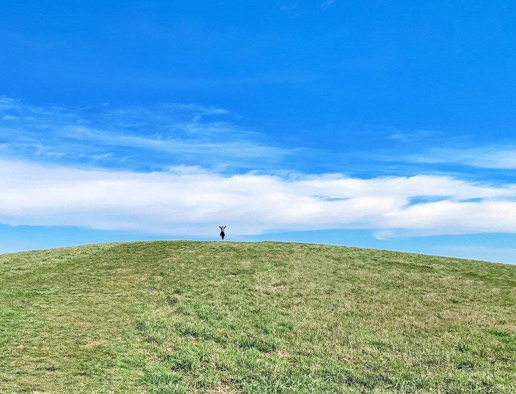 A lone figure stands atop a grassy hill under a vast blue sky with scattered clouds in Williamson County, Tennessee.