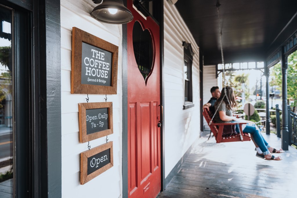 A quaint coffee shop with a vibrant red door and a welcoming porch swing where two people are enjoying their drinks in Williamson County, Tennessee.