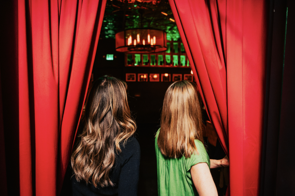 9 Unexpected Things To Do in Franklin Two women stand behind red curtains, looking into a dimly lit room with a chandelier in Williamson County, Tennessee.