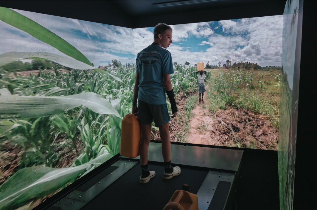 9 Unexpected Things To Do in Franklin A young boy stands on a treadmill facing a large screen showing a rural African landscape with cornfields and a dirt path in Williamson County, Tennessee.