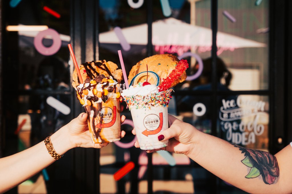 Best Family-Friendly Restaurants in Franklin Two hands holding decadent milkshakes topped with cookies and candy in front of a window in Williamson County, Tennessee.