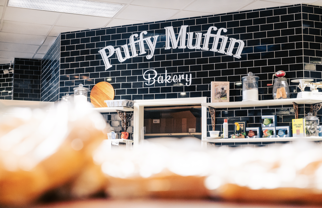 A cozy bakery with a black and white tiled wall featuring the sign 'Puffy Muffin Bakery' in Williamson County, Tennessee.