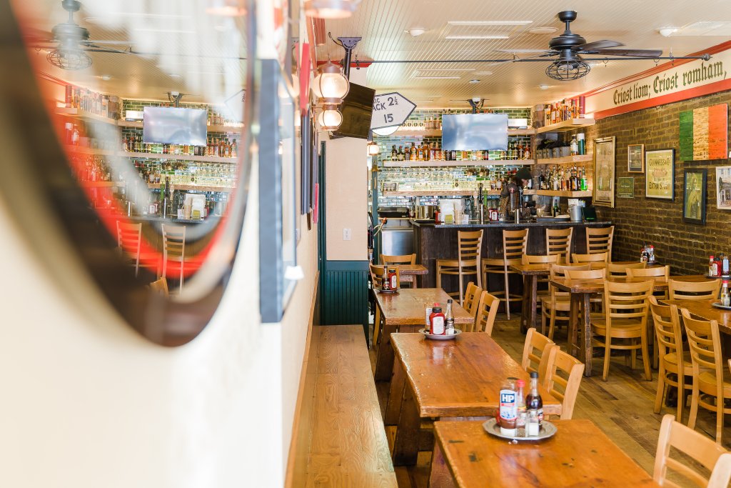 A cozy pub interior with wooden tables, chairs, and a well-stocked bar, featuring a brick wall adorned with various signs and memorabilia in Williamson County, Tennessee.