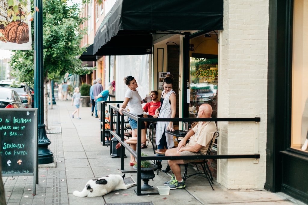 A lively street scene with people enjoying a sunny day at an outdoor cafe, while a dog rests on the sidewalk in Williamson County, Tennessee.