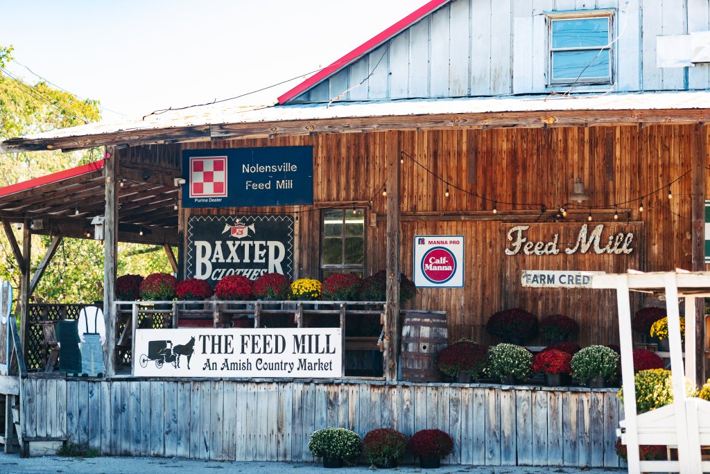 A rustic wooden feed mill building decorated with colorful potted mums in Williamson County, Tennessee.