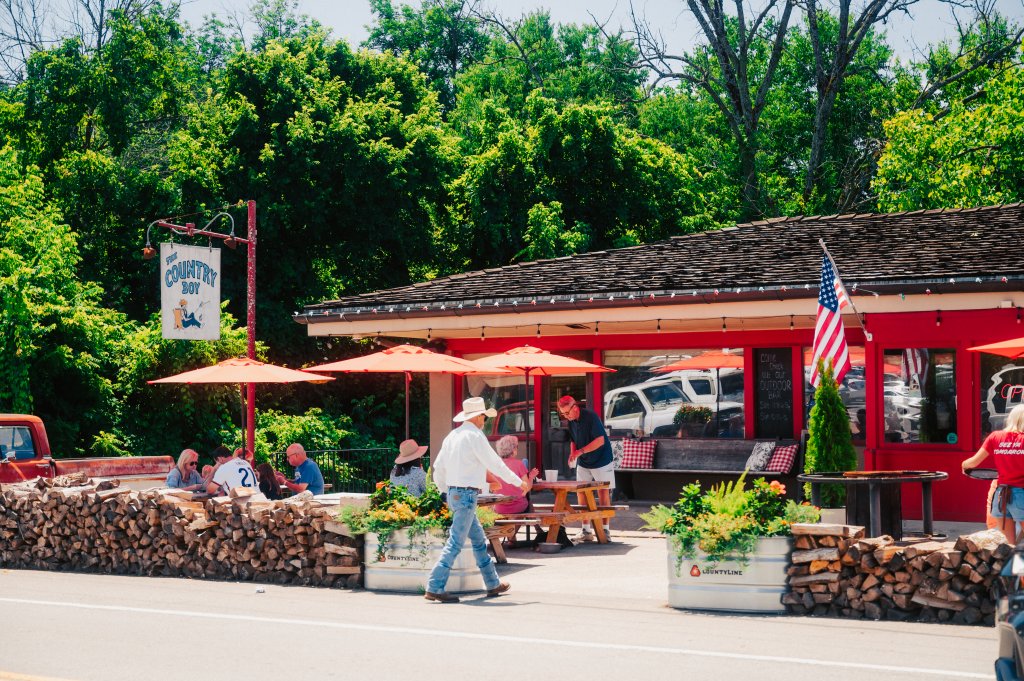 People dining on the patio of a red restaurant with a wood-stacked barrier in Williamson County, Tennessee.