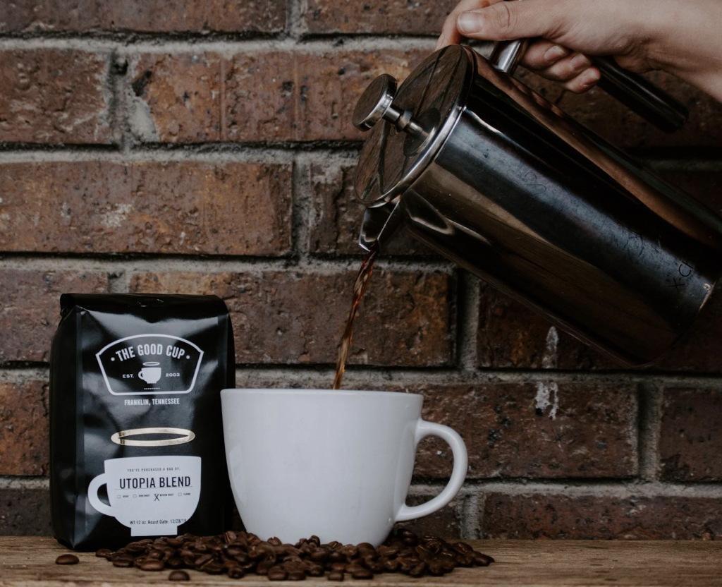 A hand pours freshly brewed coffee from a French press into a white mug next to a bag of Utopia Blend coffee beans in Williamson County, Tennessee.
