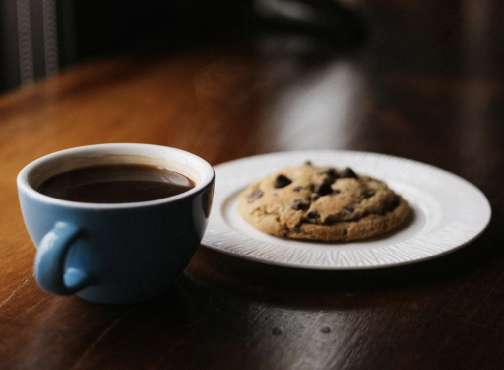 A steaming cup of black coffee sits beside a chocolate chip cookie on a white plate in Williamson County, Tennessee.