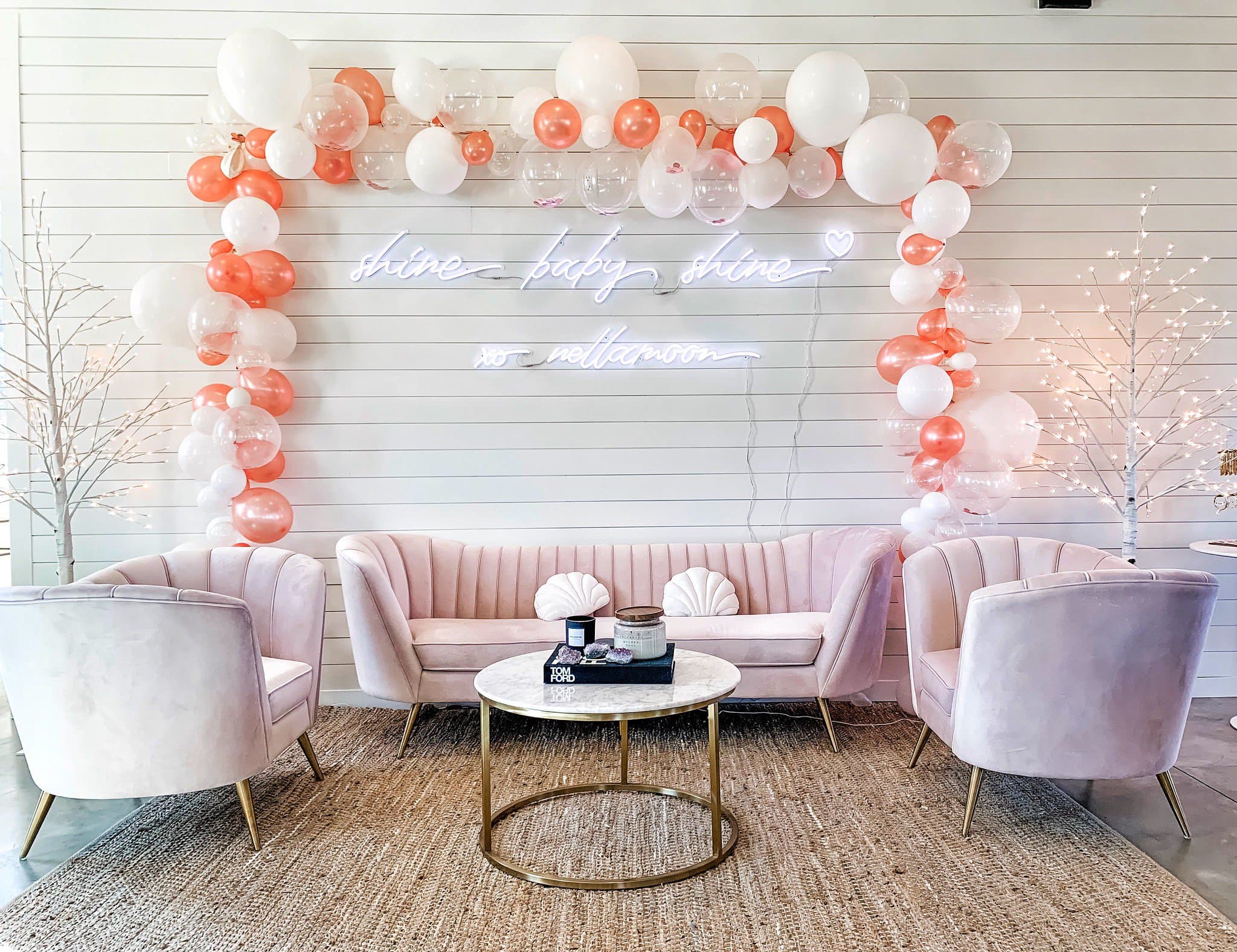 A pastel pink living room with a gold coffee table, balloon arch, and neon sign in Williamson County, Tennessee.