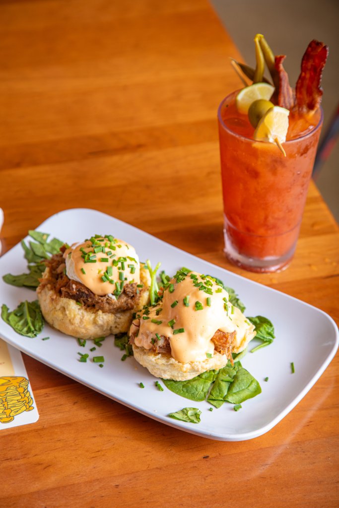 A plate of biscuits and gravy topped with poached eggs and chives, served with a glass of Bloody Mary garnished with bacon, olives, and a lemon wedge in Williamson County, Tennessee.