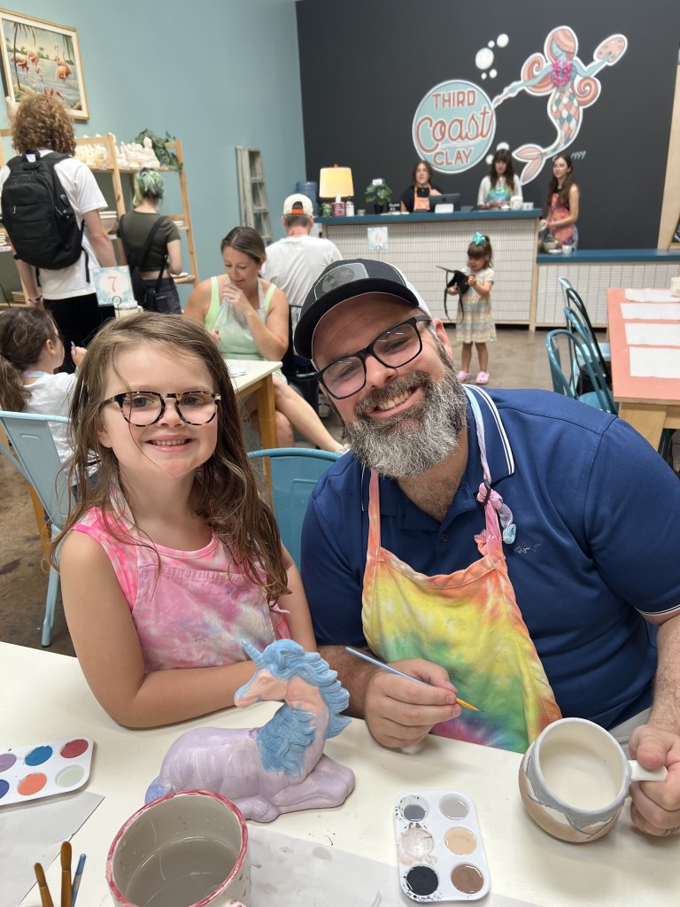 A smiling man and young girl paint a unicorn figurine at a pottery studio in Williamson County, Tennessee.