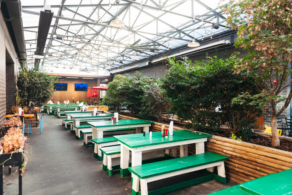 Outdoor dining area with green picnic tables, potted plants, and a glass roof in Williamson County, Tennessee.