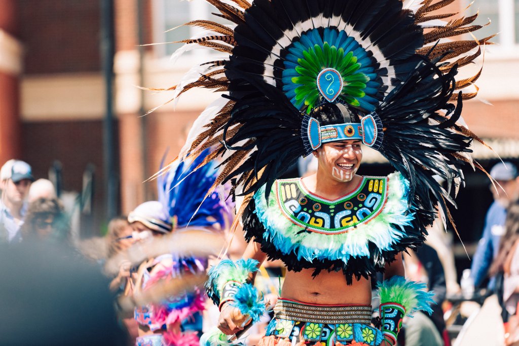 A performer in a vibrant, traditional costume with a large feathered headdress dances in a colorful parade in Williamson County, Tennessee.