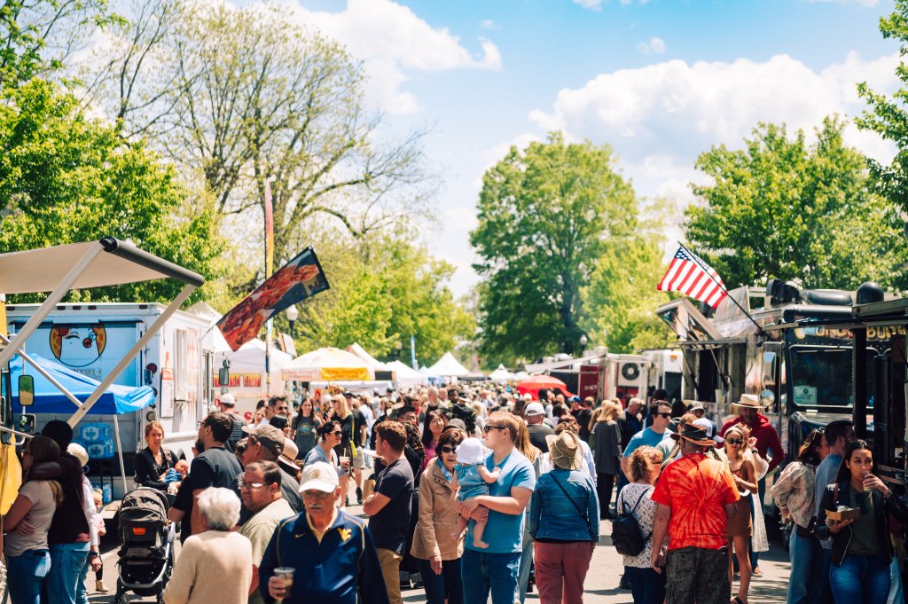 A bustling outdoor festival with food trucks, tents, and a lively crowd enjoying a sunny day under the trees in Williamson County, Tennessee.