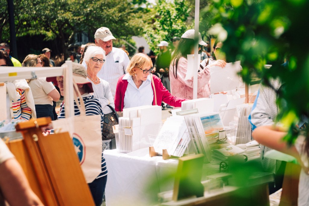 A bustling outdoor art fair with a diverse crowd of visitors browsing through various artworks and crafts displayed on tables in Williamson County, Tennessee.