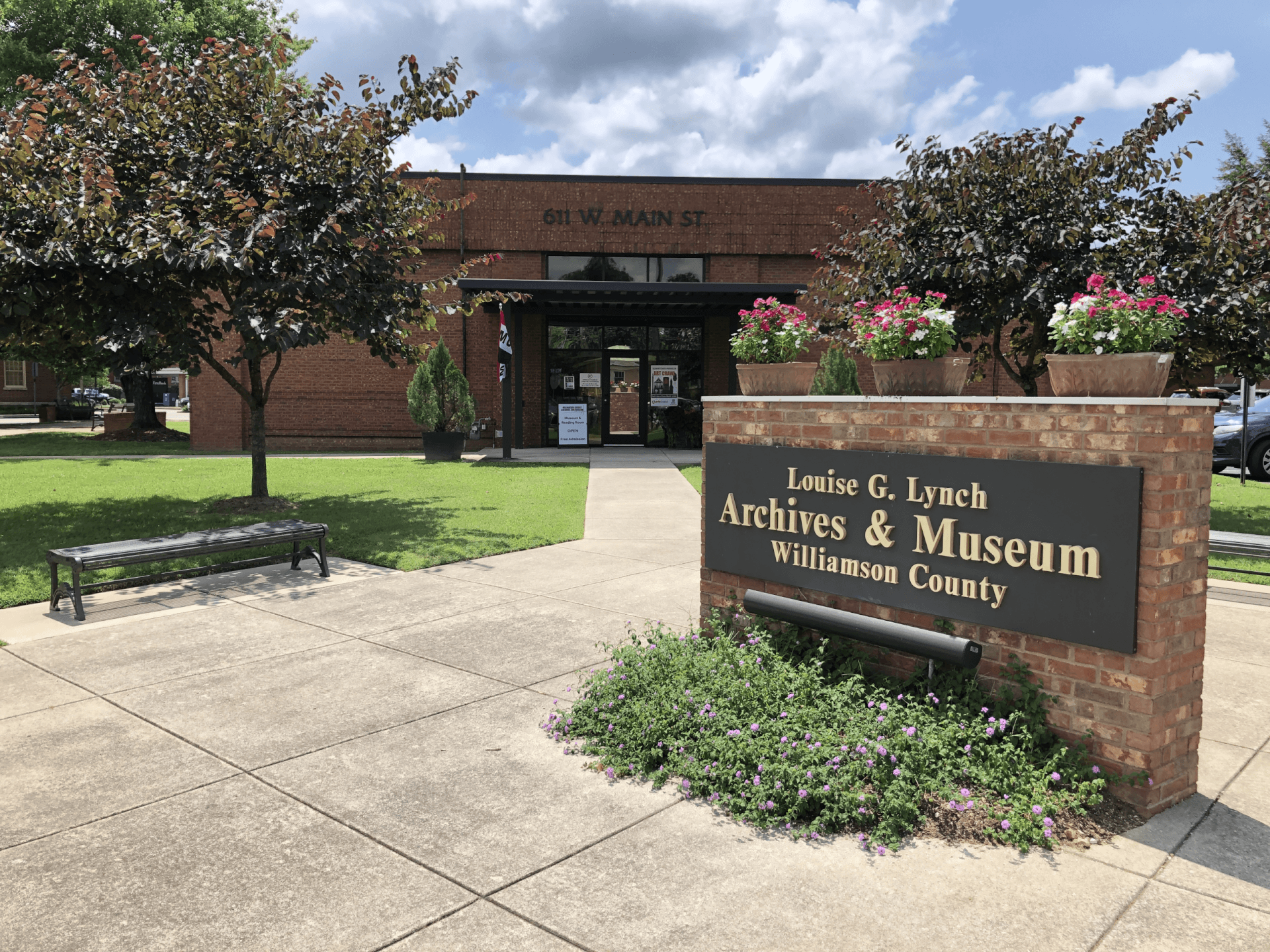 A quaint brick building with a sign reading 'Louise G. Lynch Archives & Museum, Williamson County' surrounded by lush greenery and colorful flowers in Williamson County, Tennessee.