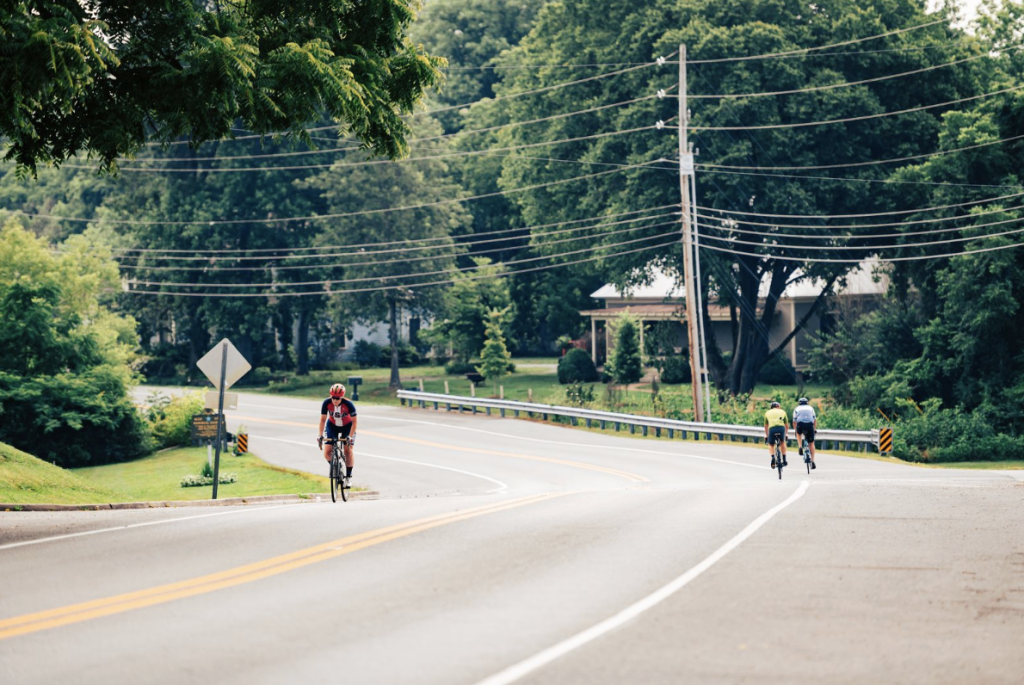 Three cyclists ride on a winding road surrounded by lush greenery and power lines in Williamson County, Tennessee.