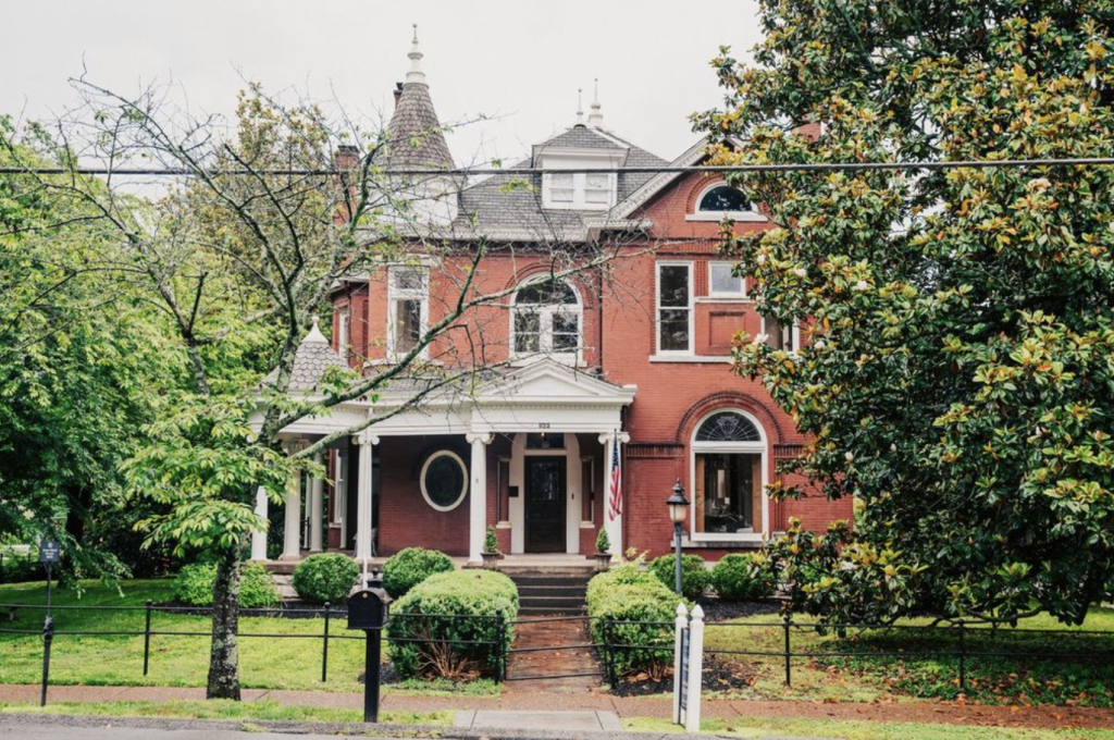 A charming red brick Victorian house with white columns and a porch, nestled among lush green trees in Williamson County, Tennessee.