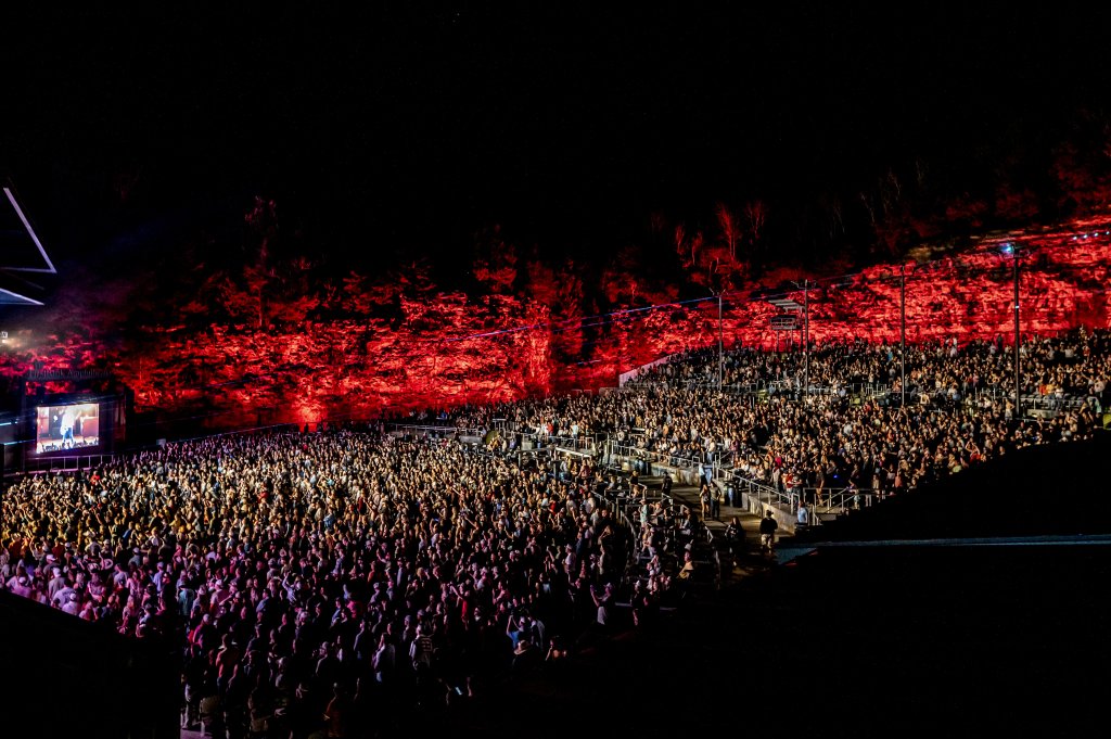 A massive crowd fills a stadium illuminated by vibrant red lights, creating a sea of people under the night sky in Williamson County, Tennessee.